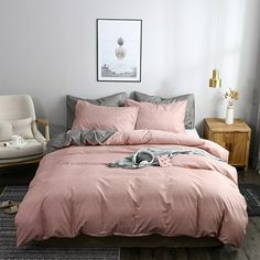 a bed with pink comforter and pillows in a room next to a chair, table and pictures on the wall