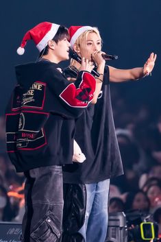 two people standing next to each other with microphones in their hands and one person wearing a santa hat