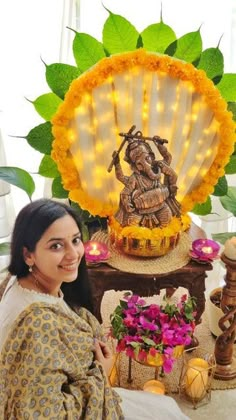 a woman sitting in front of a statue with flowers on it and lights behind her