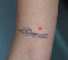 a small wave tattoo on the wrist with an orange ball in the middle of it