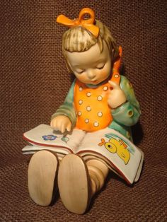 a ceramic figurine sitting on top of a brown couch holding a book and reading