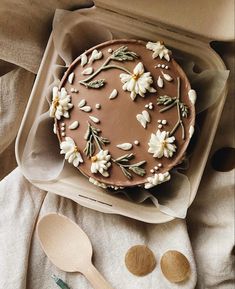 a chocolate cake with white flowers on top and spoons next to it in a box