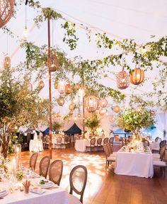 a banquet hall with tables and chairs covered in white linens, hanging lanterns and greenery