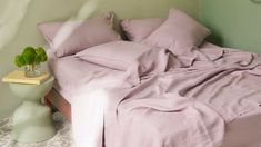 a bed with pink sheets and pillows on top of it next to a night stand