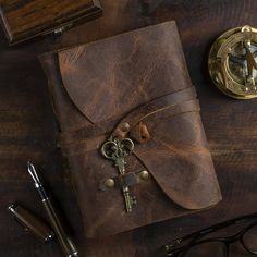 a brown leather journal sitting on top of a wooden table next to a pen and glasses