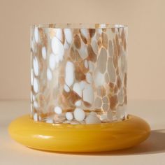 a glass candle holder sitting on top of a yellow stand with white and gold designs