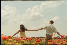 a man and woman holding hands in a field of flowers