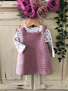 a pink crocheted dress hanging on a wooden door with flowers in the background