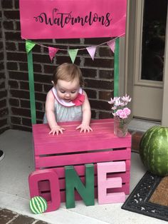 a baby sitting on top of a wooden bench next to a watermelon sign