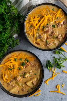 two black bowls filled with soup and cheese on top of a gray surface next to parsley