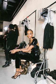 a woman sitting on a chair in front of some clothes