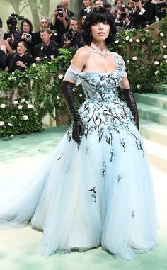 a woman in a blue and white gown standing on a green carpet with cameras around her