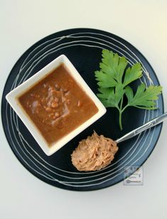 a black plate topped with a bowl of soup next to a green leafy plant