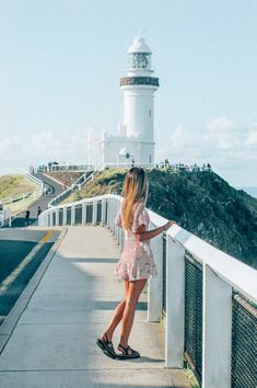 a woman standing on the side of a road near a light house