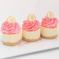 three small desserts with pink frosting and gold numbers on top are sitting on a white plate