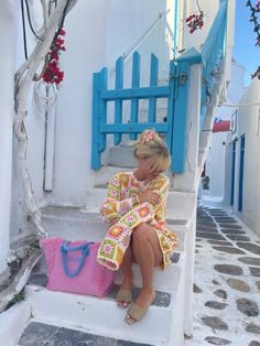 a woman sitting on the steps with a pink bag in front of her and a blue door behind her