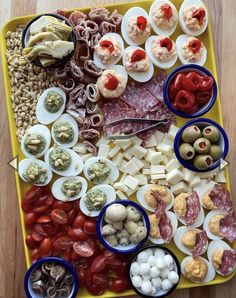 a platter filled with meats, cheeses and vegetables on top of a wooden table