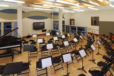 an empty room filled with lots of black chairs and musical instruments in front of a piano