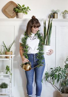 a woman is holding a potted plant and watering it with a gold watering can