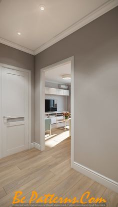 an empty living room with wood flooring and white doors leading to the kitchen area