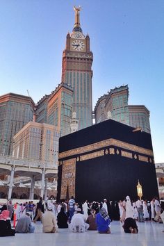 many people are praying in front of the kabab, with tall buildings in the background