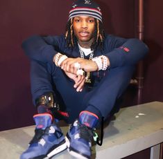 a man with dreadlocks sitting on top of a counter next to a pair of sneakers