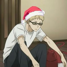 a young man wearing glasses and a santa hat sitting on the floor next to a red bag