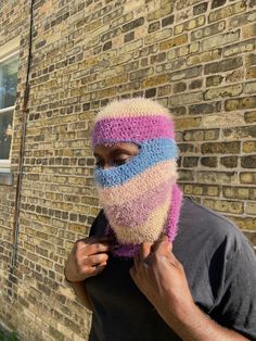 a man with a knitted mask on his face is standing in front of a brick building