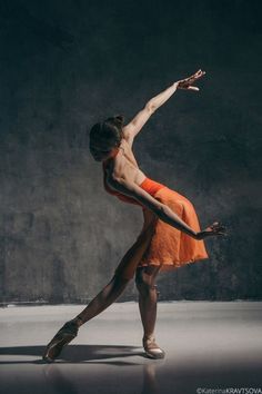 a ballerina in an orange dress is posing for the camera with her arms stretched out