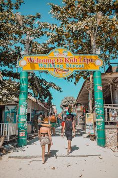 people walking under a sign that says welcome to kohlripe island resort on the beach