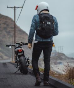 a man walking next to a motorcycle on the road