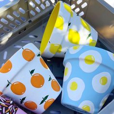 four cups with oranges on them sitting in a basket next to some napkins