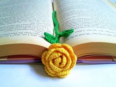 an open book with a crocheted flower on it's end and a green leaf