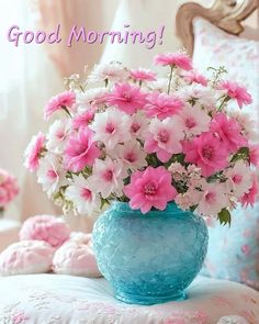 a blue vase filled with pink and white flowers on top of a bed next to pillows