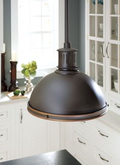 a light hanging over a kitchen counter in a room with white cabinets and cupboards