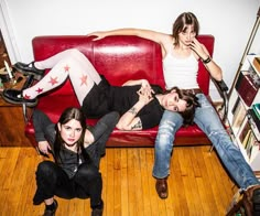 three young women laying on a red couch