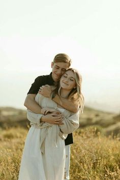 a man and woman hugging each other in the middle of a field with tall grass