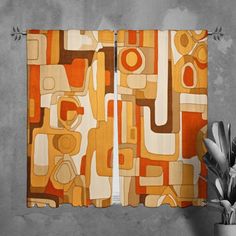 an orange and brown abstract curtain hanging on a wall next to a potted plant