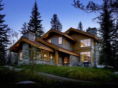 a large house sitting on top of a lush green hillside next to tall pine trees