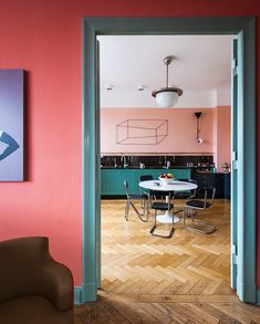 an open door leading to a kitchen and dining room with pink walls, wood floors and green accents