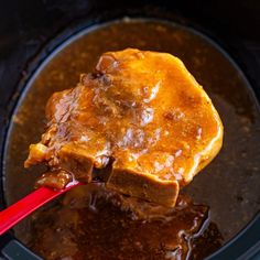 a piece of meat is being cooked in the slow cooker with a red spoon