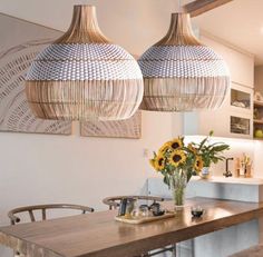 two lamps hanging over a wooden table with flowers in vases on the top and bottom