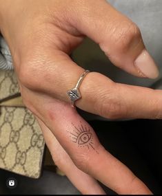 a woman's hand with a small tattoo on the middle finger and an eye ring