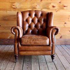 a brown leather chair sitting on top of a wooden floor next to a wood wall