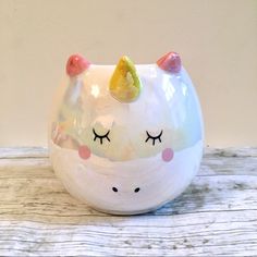 a white ceramic cup with a unicorn face and eyelashes on it's head, sitting on a wooden surface