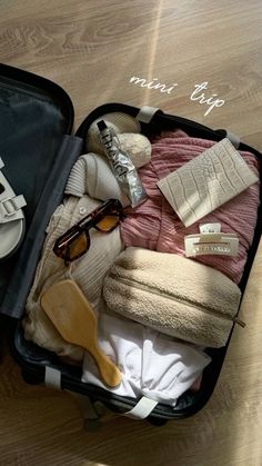 an open suitcase filled with clothes and other items on top of a wooden floor next to a pair of sunglasses