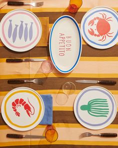 plates and utensils laid out on a striped tablecloth with lobsters, crabs, and fish