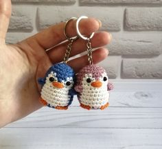 two small crocheted penguin keychains are being held by a person's hand