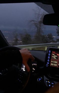 a person driving a car at night with the city lights visible in the back ground