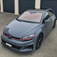 a grey volkswagen car parked in front of a garage with two garage doors on it